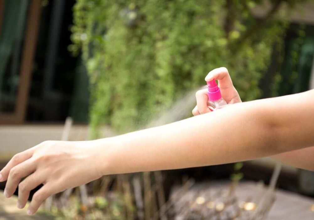 Woman spraying insect repellents on skin in the garden with spray bottle